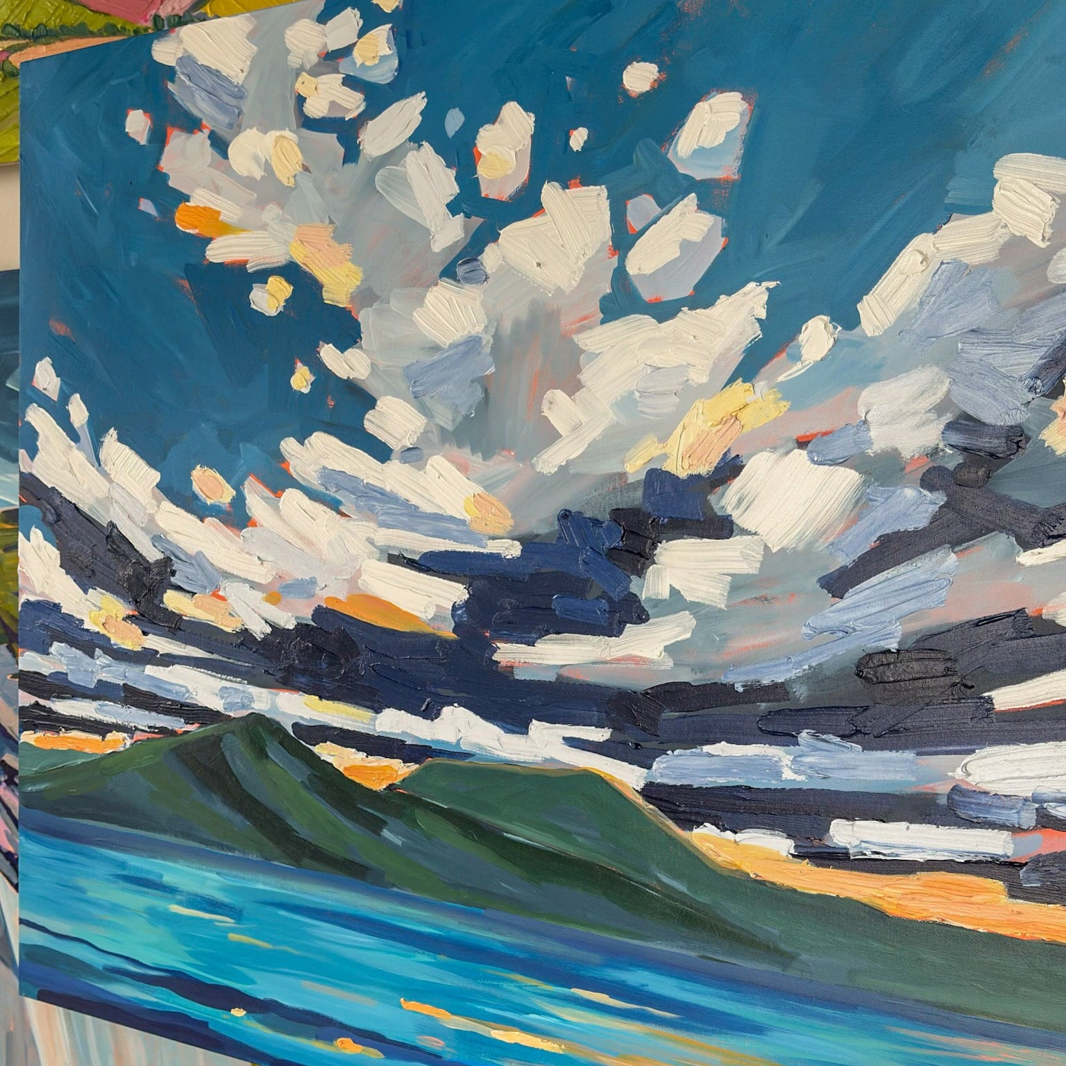 Painting of a landscape with a blue sky and green fields on an easel.